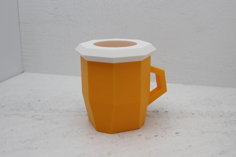May include: A geometric mug with a faceted orange body and a white lid featuring a circular opening. The mug has a sharp, angular handle and a distinct polygonal shape, presenting a modern, structured design with clean lines and a solid colour finish.