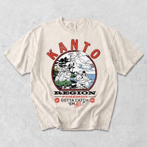 Puede incluir: Camiseta color crema con un diseño gráfico circular. El diseño presenta el texto "KANTO" en rojo y tres personajes Pokémon. El texto "REGION Pokémon GOTTA CATCH 'EM ALL!" es rojo y negro.