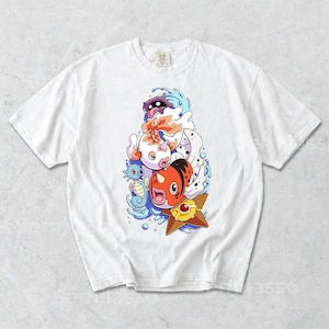 May include: White t-shirt featuring a colorful cartoon graphic of various aquatic creatures. The design includes a red and orange fish, a blue seahorse, and other stylized characters, all set against a backdrop of blue water elements.