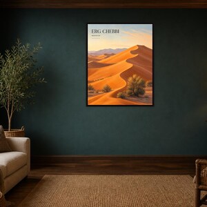 May include: A rectangular wall art print featuring a desert landscape with orange sand dunes under a pale sky. The text ERG CHEBBI and MOROCCO is printed in black at the top. The artwork is enclosed in a thin black frame and displayed on a dark wall.