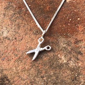 May include: A silver chain necklace with a small silver scissor pendant.