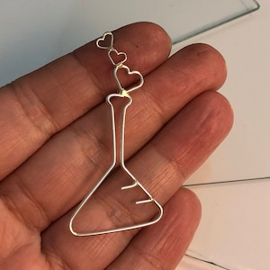 May include: A silver wire sculpture of a beaker with three small hearts attached to the top.