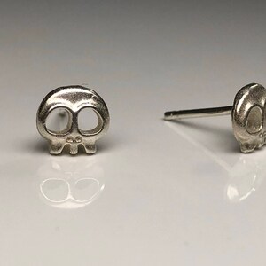 May include: A pair of silver skull stud earrings. The skull design is simple and minimalist, with no additional details.