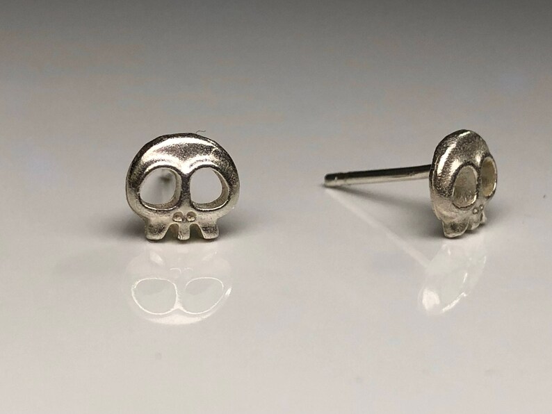 May include: A pair of silver skull stud earrings. The skull design is simple and minimalist, with no additional details.