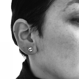 May include: A person wearing a black turtleneck sweater with a small silver skull earring in their left ear.