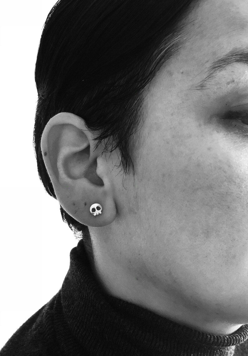 May include: A person wearing a black turtleneck sweater with a small silver skull earring in their left ear.