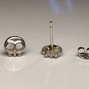 May include: A pair of silver skull stud earrings with a post and butterfly backing.