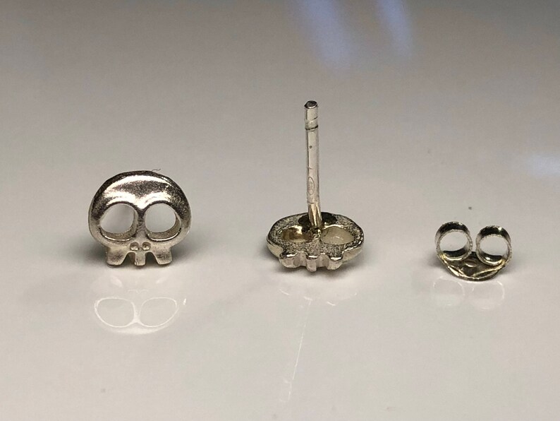 May include: A pair of silver skull stud earrings with a post and butterfly backing.