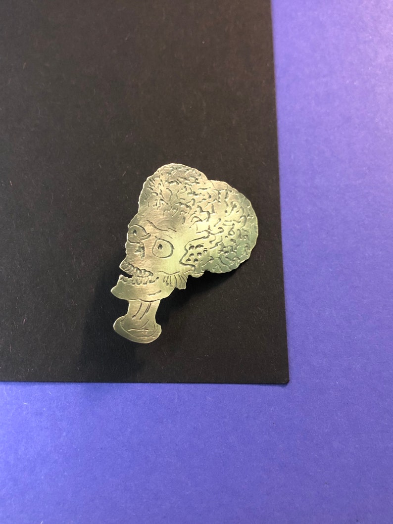 Pode incluir: Pin de metal prateado com um perfil detalhado de um alien&iacute;gena de desenho animado com uma cabe&ccedil;a grande e um corpo pequeno. O alien&iacute;gena tem uma cabe&ccedil;a grande e redonda com uma superf&iacute;cie texturizada e um corpo pequeno e fino com um pesco&ccedil;o longo.
