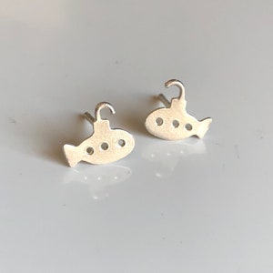 May include: A pair of silver earrings shaped like submarines. Each earring has three small circles on the side, representing portholes.