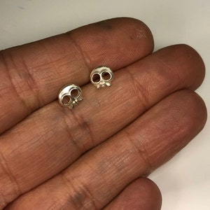 May include: A pair of silver skull stud earrings. The earrings are small and delicate, and they have a simple, minimalist design.