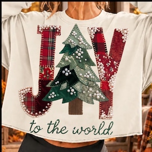 May include: A cream-colored long-sleeve sweatshirt featuring a large applique design spelling JOY. The letters J and Y are made of red plaid fabric, while the O is a green fabric Christmas tree. All letters are embellished with white pearls.