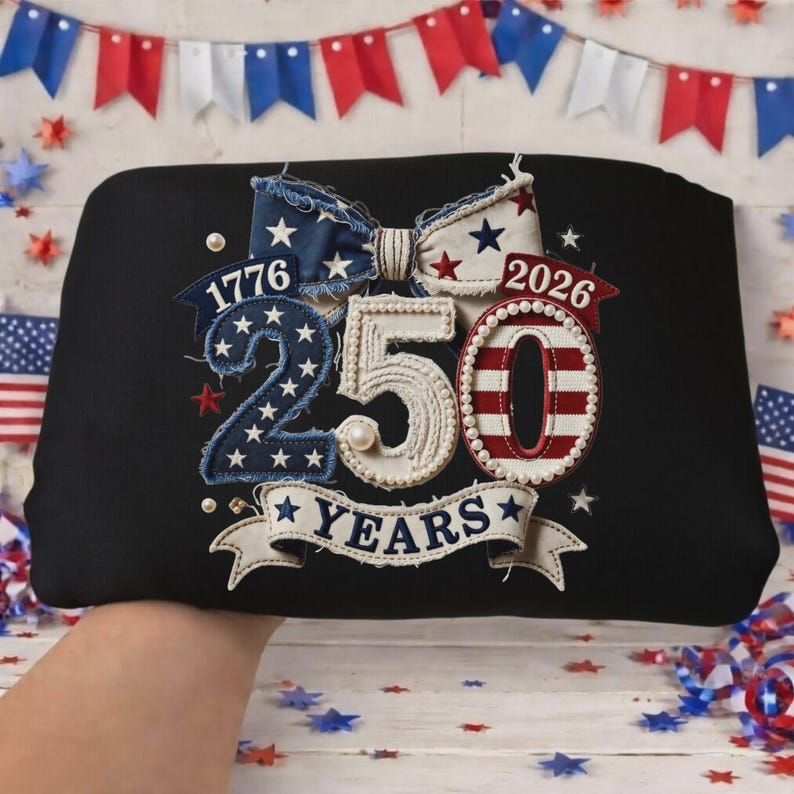 May include: Black tote bag with an embroidered design celebrating 250 years. The design includes the years 1776 and 2026, a bow, the number 250, and the word "YEARS" on a banner, all in patriotic colors.
