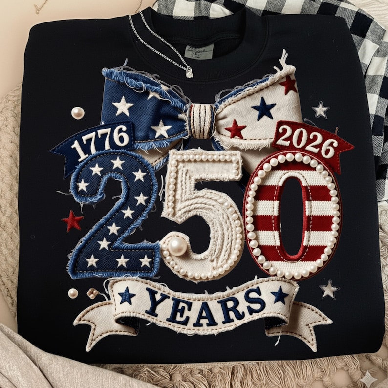 May include: Black sweatshirt with a patriotic design celebrating 250 years. Features a bow with stars and stripes, the numbers "1776" and "2026", and the number "250" with the word "YEARS" on a banner. Embellished with pearls and stars.