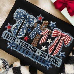 May include: Black decorative pillow with embroidered patriotic design. Features a cross, bows, and stars in red, white, and blue. Text reads "Faith, Freedom, 1776-2026, 250 Years."