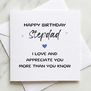 May include: A white birthday card with the message "Happy Birthday Stepdad" in black script. The card includes a blue heart and the words "I love and appreciate you more than you know." The card is placed on top of a white envelope.