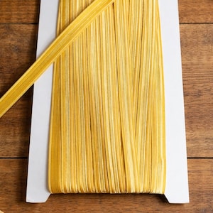 May include: A spool of yellow ribbon with a subtle sheen, presented on a white card. The ribbon is tightly wound, with a single length extending outwards. Ideal for crafts, gift wrapping, and decorative projects.