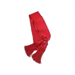 Pode incluir: Uma faixa vermelha brilhante com duas borlas a condizer. A faixa é feita de um material liso, possivelmente acetinado. As borlas são feitas de fios bem enrolados, adicionando textura ao design. O item é provavelmente usado para fins cerimoniais ou decorativos.