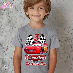 May include: A gray t-shirt featuring a red Lightning McQueen car graphic with the number 3, checkered flags, and the text "Chandler Birthday Boy". The shirt is designed for a child's birthday celebration.