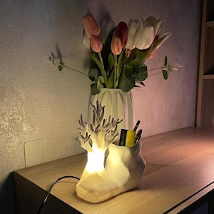 Puede incluir: Lámpara decorativa con diseño de coral, que emite una luz cálida. Se encuentra sobre una superficie de madera, junto a un jarrón blanco lleno de tulipanes rosas, rojos y blancos.