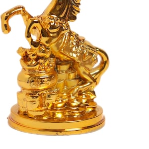 Könnte beinhalten: Goldene Pferdfigur in aufsteigender Pose, mit aufwendigen Details. Das Pferd steht auf einem Sockel mit Goldmünzen. Die Figur besteht aus einem glänzenden, reflektierenden Material.