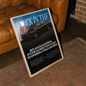 May include: A framed poster with the text "STUCK IN THE 80s" and "BUY AN OLD SHITBOX, IT'S THE CLOSEST YOU'LL GET TO OWNING A TIME MACHINE". The poster features a black car and is set against a blue background.