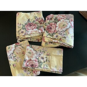 May include: A set of four bedding pieces featuring a pale yellow background with a floral pattern of large pink and white roses, smaller purple blossoms, and green leaves. The collection includes two larger folded sheets and two pillowcases.