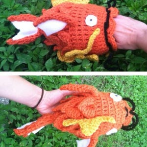 May include: A handmade orange crochet fish with white accents and a yellow fin. The fish has a large open mouth and a single white eye. The fish is a novelty item.
