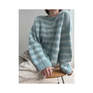 May include: A light blue knit sweater with a round neckline and long sleeves. The sweater features a striped pattern with openwork details. The sleeves are cuffed at the wrists. The sweater is made of a soft, textured yarn.