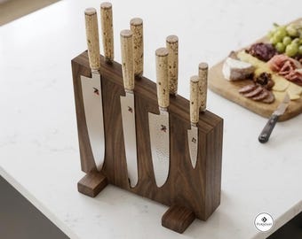 May include: A dark brown wooden magnetic knife block holding six stainless steel kitchen knives with light-colored, speckled cork-like handles. The knives feature silver blades, some with a hammered finish, and a small logo on the blade surface.