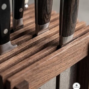 May include: A wooden knife block with a dark brown grain pattern holding several kitchen knives. The knives feature dark, textured handles with silver bolsters. A small white circular logo with the text Furniast is visible on the side.