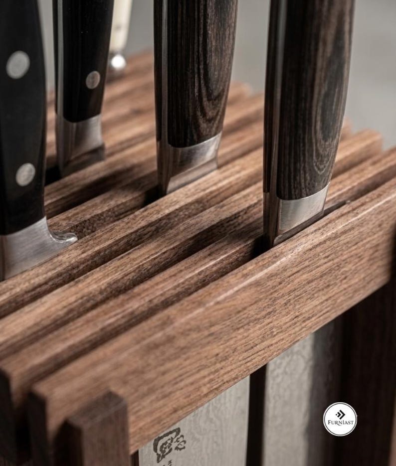 May include: A wooden knife block with a dark brown grain pattern holding several kitchen knives. The knives feature dark, textured handles with silver bolsters. A small white circular logo with the text Furniast is visible on the side.