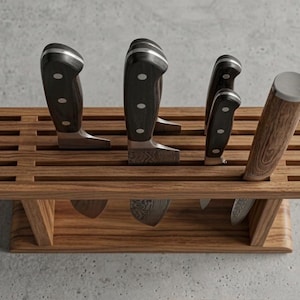May include: A rectangular wooden knife block with horizontal slats holding four kitchen knives. Three knives feature black handles with silver rivets, while the fourth knife has a light brown wood-grain handle with a silver metal end cap.