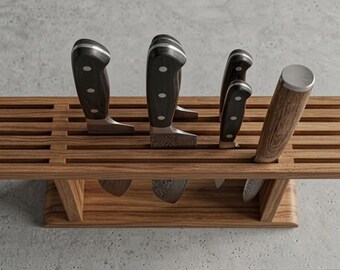 May include: A rectangular wooden knife block with horizontal slats holding four kitchen knives. Three knives feature black handles with silver rivets, while the fourth knife has a light brown wood-grain handle with a silver metal end cap.