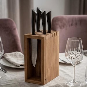 May include: A rectangular wooden knife block with a hollow center, holding four kitchen knives with dark, textured handles and patterned metal blades. The block is constructed from light brown wood with visible grain, featuring vertical slots on top.