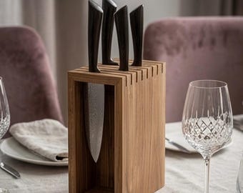 May include: A rectangular wooden knife block with a hollow center, holding four kitchen knives with dark, textured handles and patterned metal blades. The block is constructed from light brown wood with visible grain, featuring vertical slots on top.