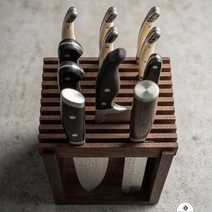 May include: A square wooden knife block with horizontal slats holding several kitchen knives with black and cream-colored handles. The knives feature metallic bolsters and textured blades. The logo Furniast is visible in the bottom right corner.