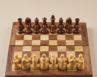 May include: A folding wooden chess set featuring a board with alternating light and dark brown squares. The set includes a full complement of dark brown and light beige wooden chess pieces arranged in their starting positions on the board.