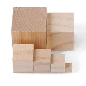 Op de afbeelding: Een verzameling onafgewerkte houten blokken van verschillende formaten, gerangschikt in een trapsgewijs patroon. De blokken zijn rechthoekig en gemaakt van lichtgekleurd hout, met de natuurlijke nerf zichtbaar. De opstelling suggereert een bouw- of stapelspeelgoed.