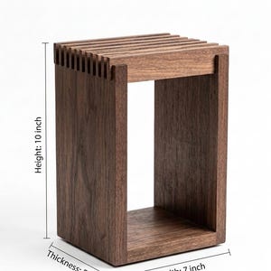 May include: A rectangular dark brown wooden stool with a slatted top surface. The structure features vertical side panels and a solid base. Dimensions are clearly labeled as 10 inches in height, 7 inches in width, and 5 inches in thickness.