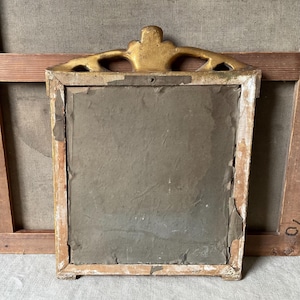 May include: Back of a vintage rectangular framed artwork. The frame is painted white with gold accents at the top. The artwork is covered with a gray paper backing. The frame is set against a neutral background.