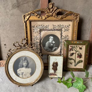 May include: A collection of antique picture frames in various shapes and sizes. The frames are gold-toned and ornate, with detailed carvings. The images inside are black and white portraits and botanical prints, creating a vintage aesthetic.