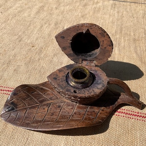 Peut inclure: Un encrier vintage en bois en forme de feuille, avec un couvercle à charnière et un pot d'encre en laiton. L'encrier est en bois brun foncé et présente des détails sculptés. Le couvercle est ouvert, révélant le pot d'encre.
