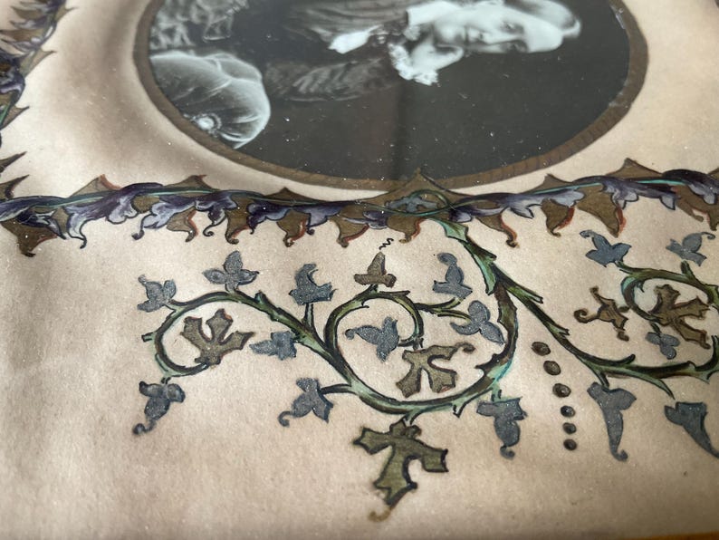 May include: Close-up of a vintage photograph in a decorative frame. The frame features a cream-colored background with a detailed floral design in green, blue, and brown. The photograph is in a circular frame with a gold border.