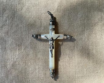 May include: A silver and mother-of-pearl cross pendant. The cross features a silver figure of Jesus Christ and the inscription INRI. The cross has ornate silver detailing on the ends and a loop for hanging.