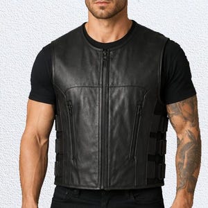 May include: A black leather waistcoat featuring a central vertical zip closure, two vertical zipped pockets on the front, and three adjustable side straps with buckles on each side. The waistcoat has a round neckline and a smooth, matte finish.