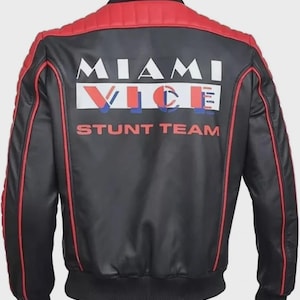 May include: Black bomber jacket with red accents on the shoulders and trim. The back features the words "MIAMI VICE STUNT TEAM" in white and red lettering. The jacket has a ribbed collar and cuffs.
