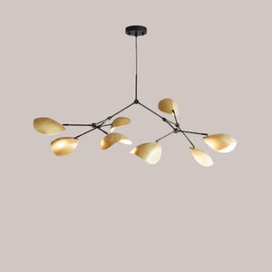 May include: Contemporary chandelier featuring a black frame and gold leaf-shaped shades. The light fitting has multiple arms extending from a central point, each holding a leaf-shaped shade. The shades are a warm gold colour, and the fixture hangs from a black ceiling mount.