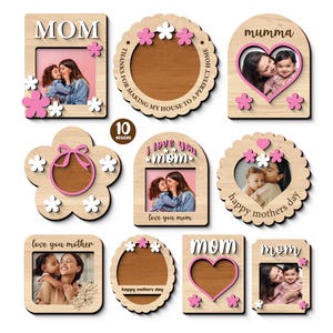 Könnte beinhalten: Eine Sammlung von zehn Holz-Fotorahmen in verschiedenen Formen, darunter rechteckige, kreisförmige und florale Designs. Die Rahmen zeigen ausgeschnittene Texte wie "MOM" und "love you mom" und sind mit rosa und weißen floralen Akzenten verziert. Jeder Rahmen enthält ein Foto.