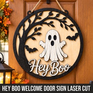 Pode incluir: Uma placa de porta circular de madeira com uma silhueta de árvore preta cortada a laser e dois morcegos sobre um fundo de madeira clara. Um fantasma branco está centrado acima do texto em letra cursiva branca que diz Hey Boo. Corda de juta.